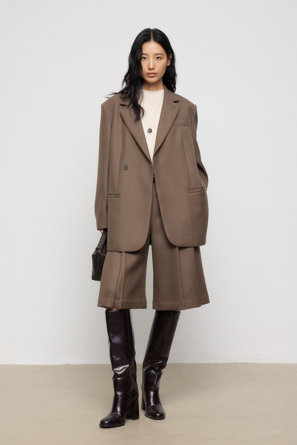 Woman wearing a brown suit with black knee-high boots on a plain background