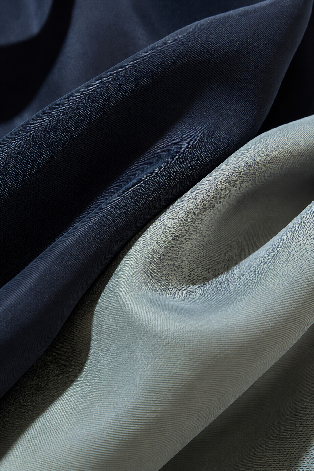 Close-up of draped fabric in two colors: a dark navy blue and a muted sage green, showing the texture and sheen of the material.
