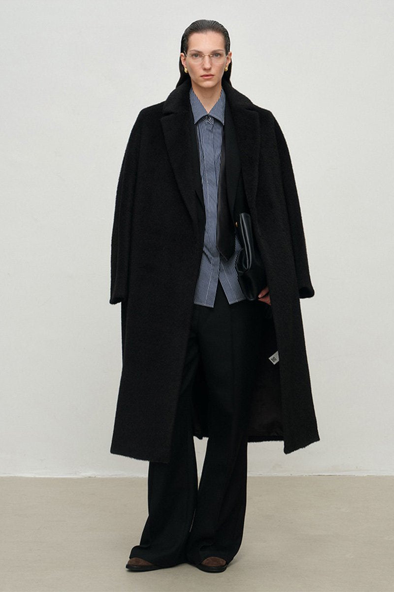 Person wearing a long black coat over a gray outfit on a plain background