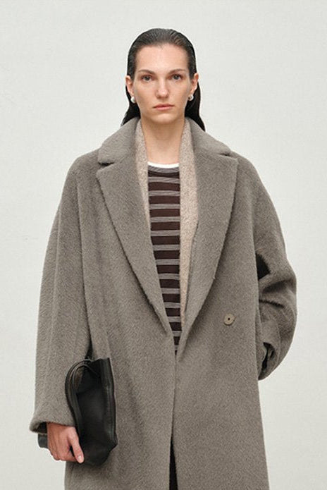 Person wearing a long gray coat and brown pants against a white background