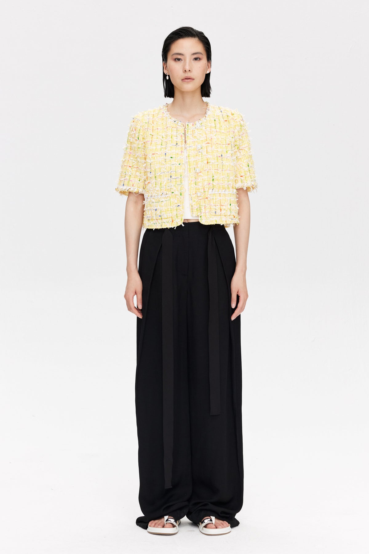 Woman wearing a yellow textured top and black wide-leg pants on a white background