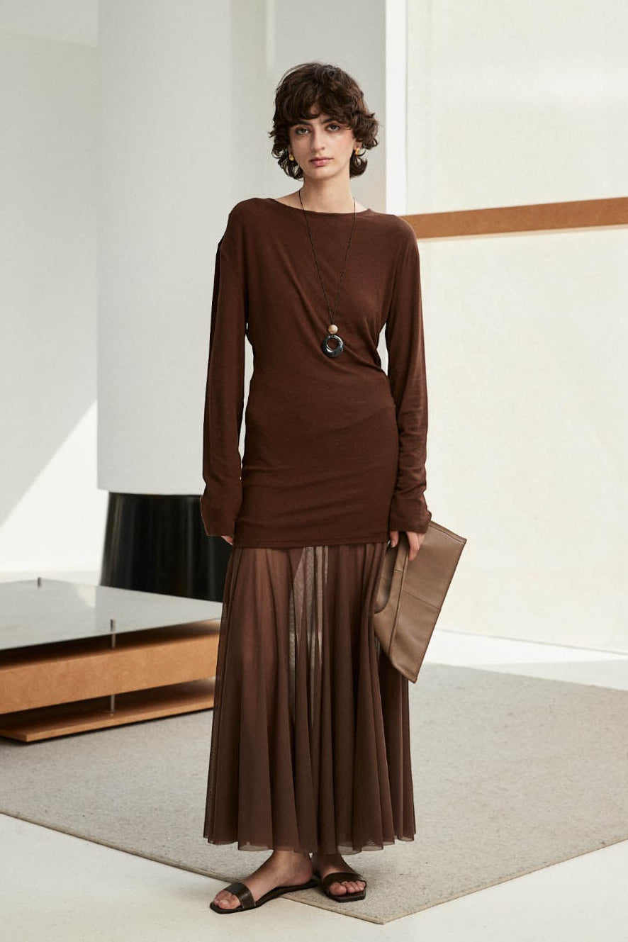 Woman wearing a brown dress with a sheer overlay in a minimalistic room.