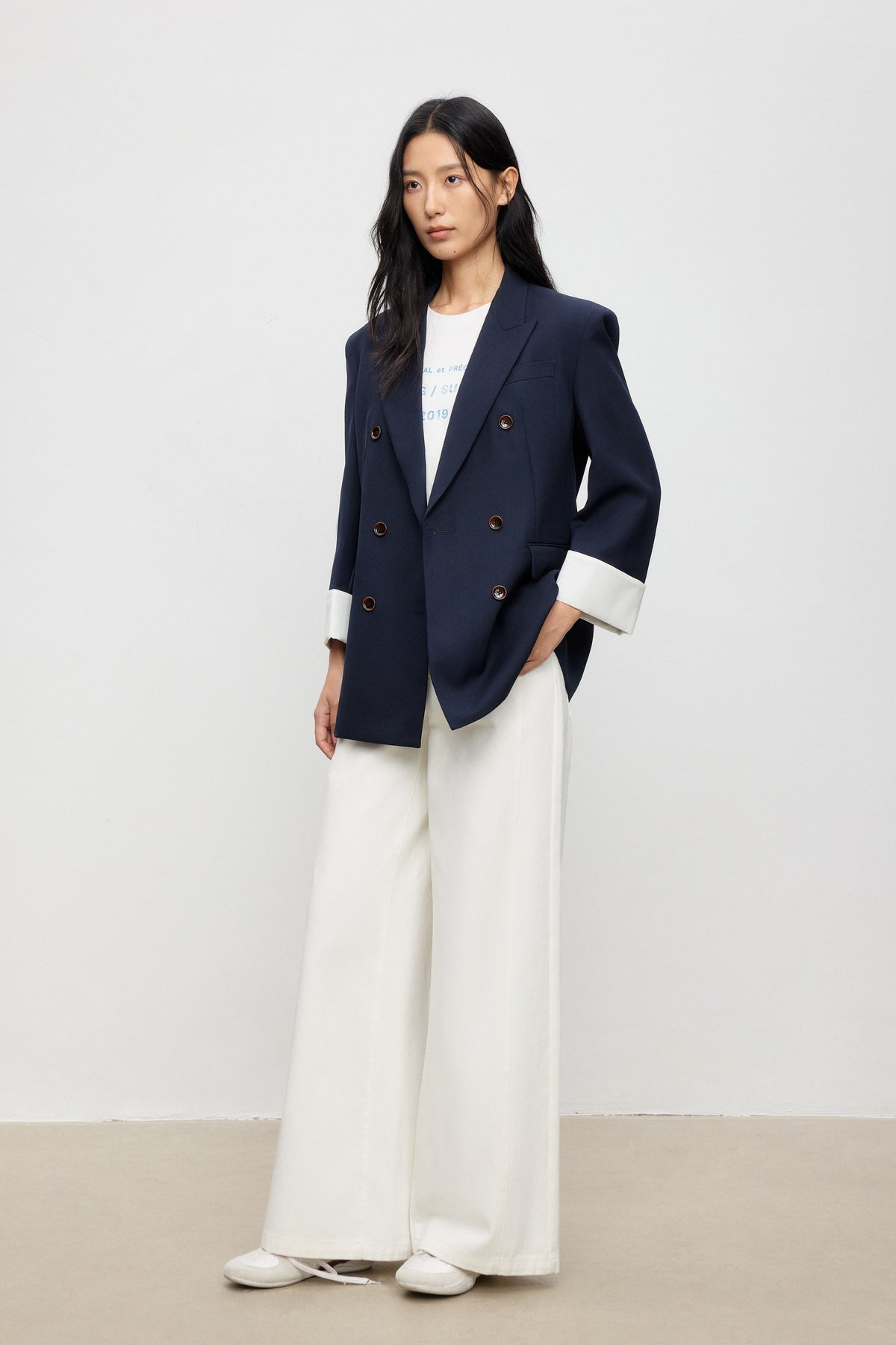 Woman wearing a navy blazer and white pants against a plain background