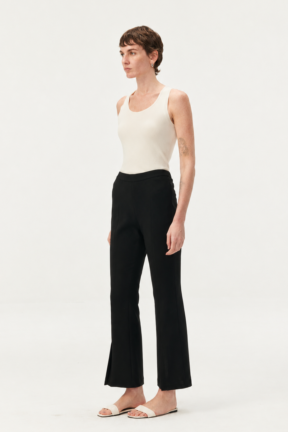 A model wearing black wide-leg cropped pants and a cream ribbed tank top, standing against a plain white studio background.