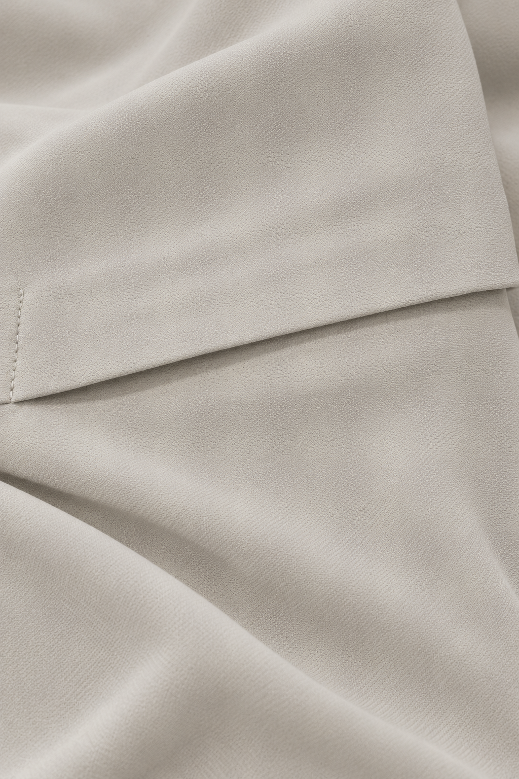 A close-up of draped light beige fabric with a visible fold and subtle texture.