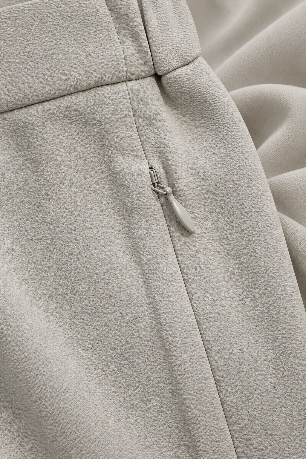 Close-up of a light beige or off-white fabric garment, showing a zipper detail and soft folds.