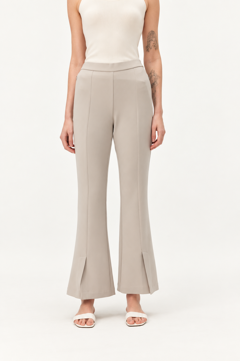 A model wearing a pair of light beige wide-leg cropped pants with front slit details at the hem, paired with a cream sleeveless top and white slide sandals, against a plain white studio background.