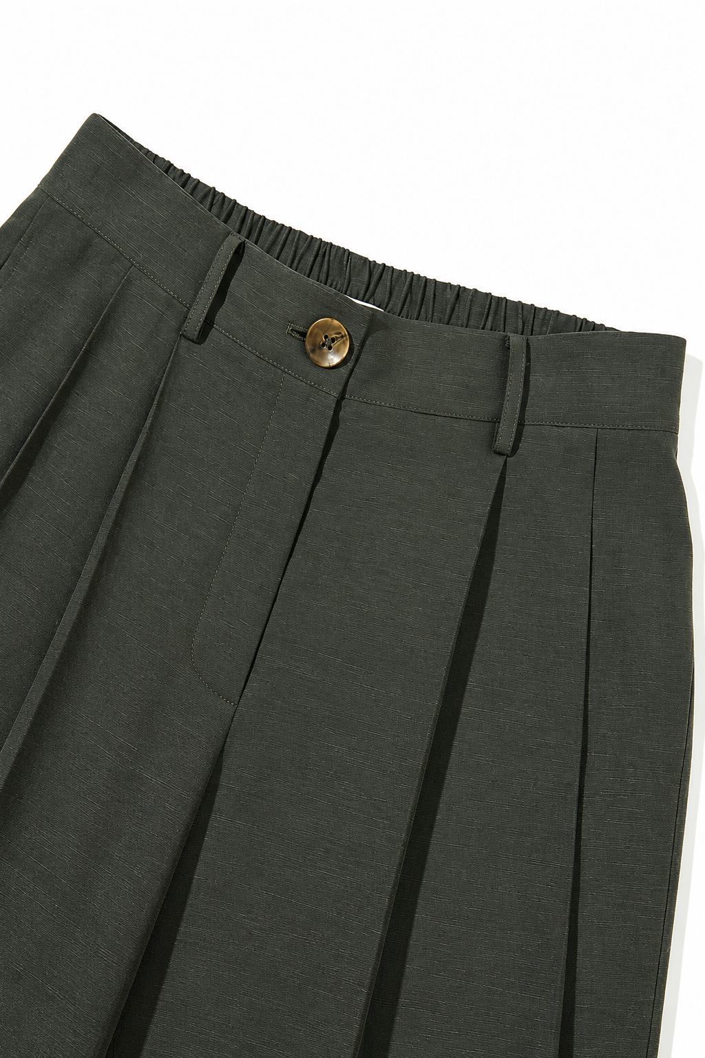 Close-up of dark olive green pleated trousers showing the waistband with an elasticized back, a single brown button, and the front pleats on a white background.