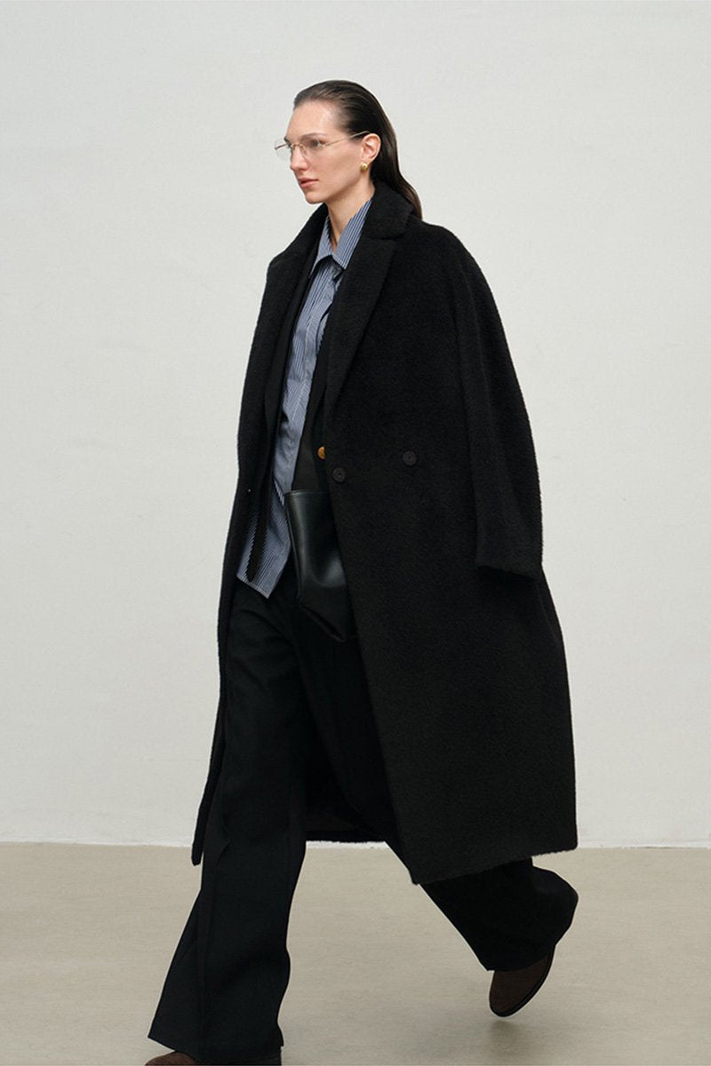 Person wearing a long black coat and glasses on a plain background