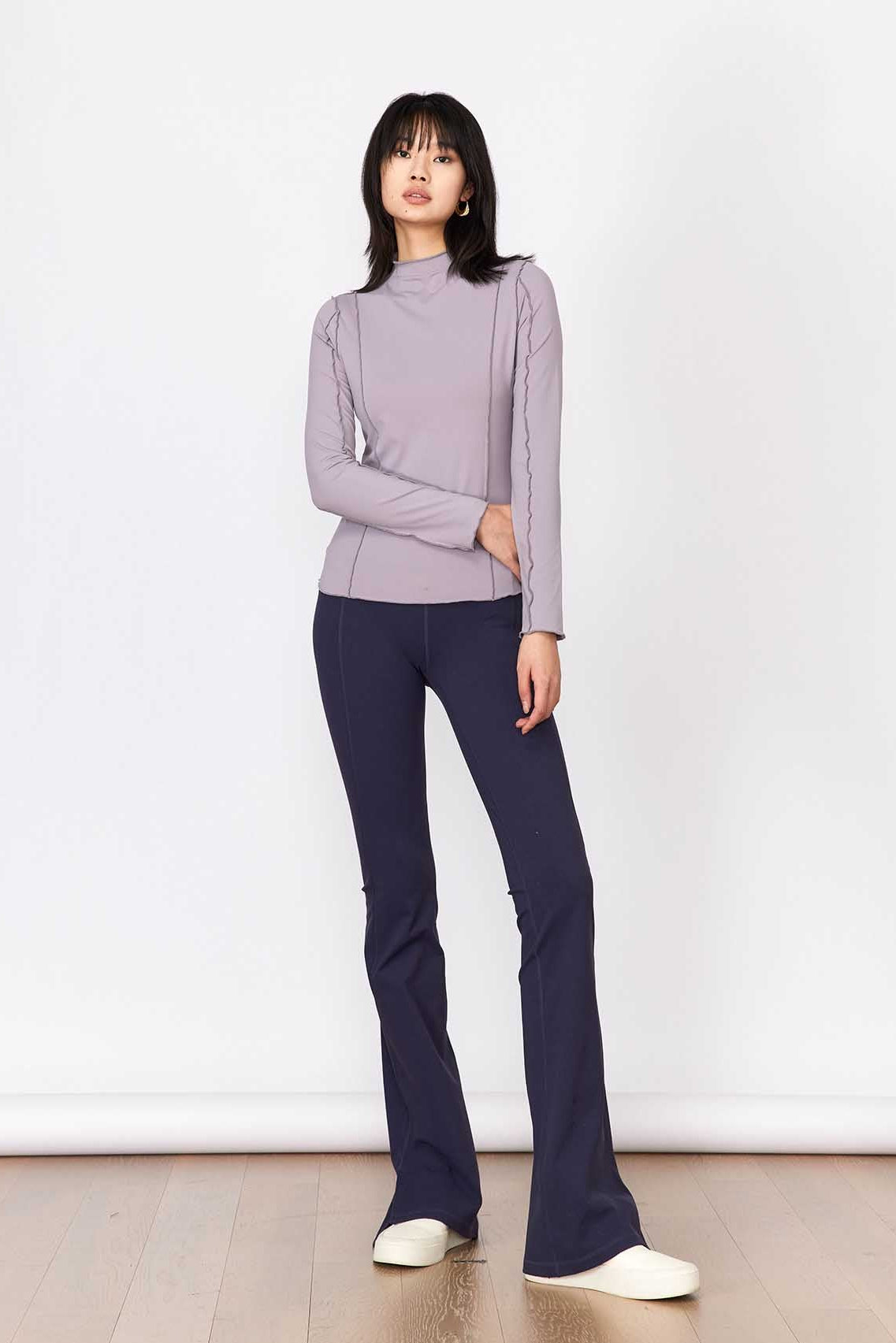 Woman wearing a light purple sweater and dark blue jeans against a white background