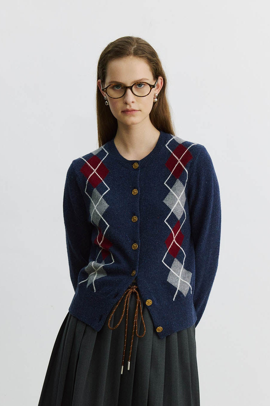 Woman wearing a blue argyle cardigan over a black skirt with a white background