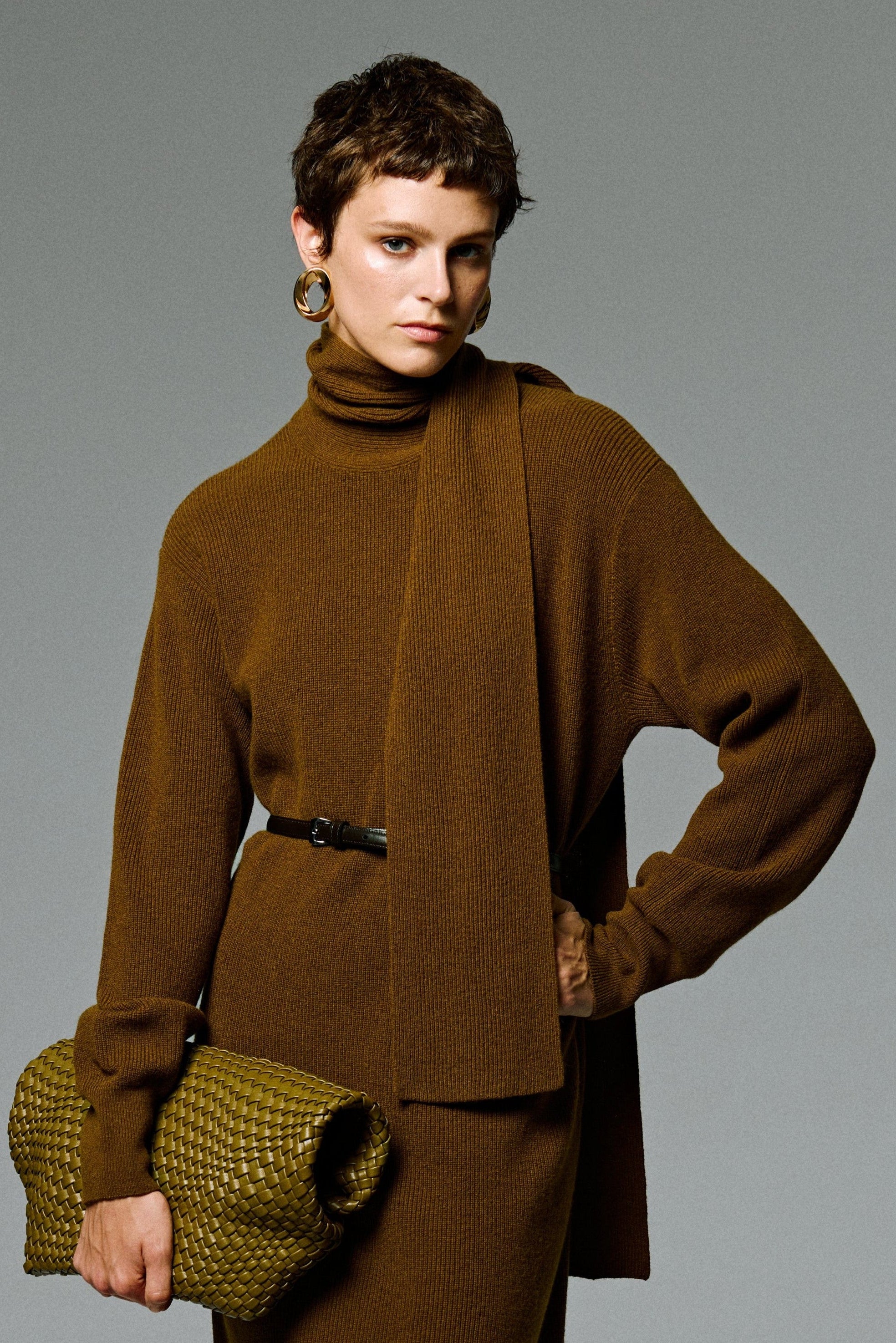 Person wearing a brown knit dress with a matching bag on a gray background
